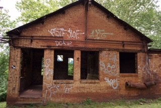 Photo of an abandoned brick building with missing windows and spray-painted graffiti on the sides