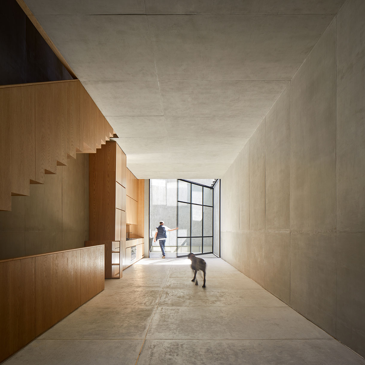 Man walks through concrete and wood room followed by a dog 