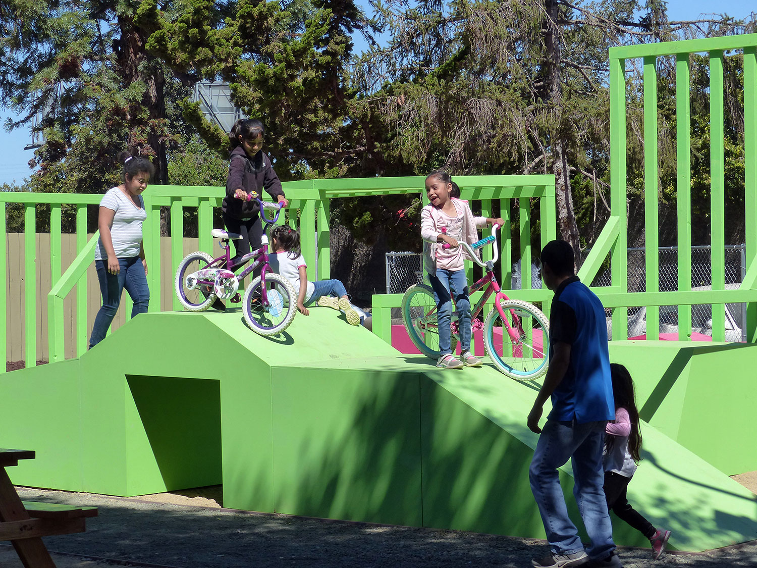 children biking and climbing on green outdoor play structure
